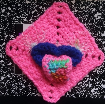 pink crocheted square with blue lips and real lip ring